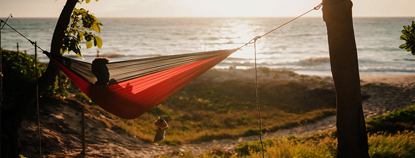 person lounging in hammock at the beach